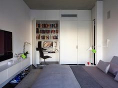 a room with a bed, desk and bookshelf next to a tv on a wall