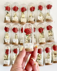 a person holding up a bottle with flowers in it next to other bottles filled with gold flakes