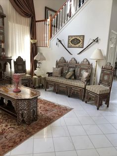 a living room filled with furniture next to a stair case in a home setting that has white tiles on the floor and walls