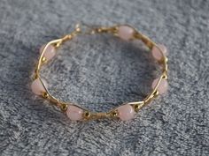 a gold bracelet with pink beads on top of a gray carpeted floor and a black bead around the clasp