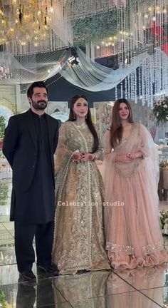 three people standing next to each other in front of a chandelier