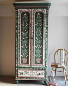 an armoire painted in green and pink with flowers on the door, next to a chair