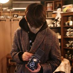 a man holding an old fashioned camera in his hands while standing next to shelves full of cameras