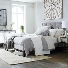 a bedroom with white walls and grey bedding, rugs and artwork on the wall