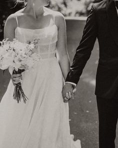 a bride and groom holding hands while walking down the street in black and white photo