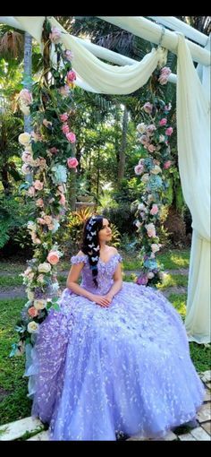 a woman in a purple dress sitting on a flower covered bench with flowers around her