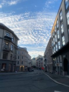 an empty city street with buildings on both sides and clouds in the sky above it