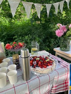 a table topped with a cake covered in strawberries next to cups and vases