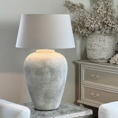 a large white vase sitting on top of a table next to a lamp and dresser