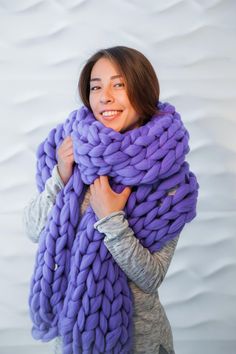 a woman holding a giant chunky purple blanket in front of her face and smiling at the camera