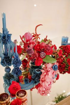 a vase filled with lots of red and blue flowers next to candles on top of a table