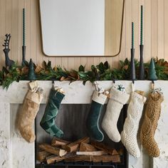 stockings hanging from the fireplace in front of a mirror with candles and greenery on it