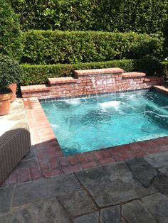 a small swimming pool surrounded by greenery and brick pavers with a waterfall running into it