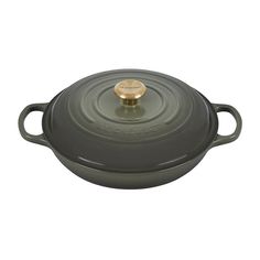 a round casserole with a gold knob on the top and bottom, sitting in front of a white background