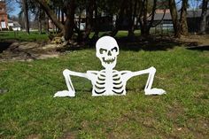 a skeleton sitting on the grass in front of some trees