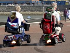 two people riding three wheeled cars with coca cola on the back and one person in a wheel chair behind them