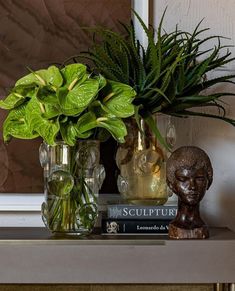 two vases filled with green plants sitting on top of a table next to a book