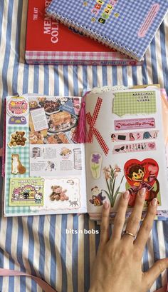 a person's hand is holding an open book on a bed with striped sheets