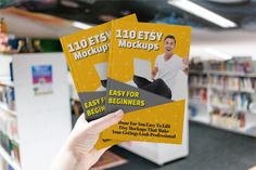 a person holding up two flyers in front of a book shelf with books on it