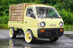 a small yellow truck parked on the side of a road with trees in the background