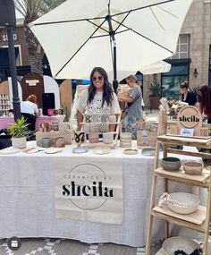 a woman is standing behind a table with bowls and cups on it at an outdoor market