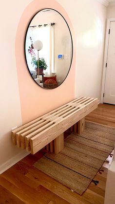 a wooden bench sitting in front of a round mirror on the side of a wall