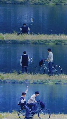 three people riding bikes next to a body of water with grass on the ground and trees in the background