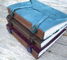 three books stacked on top of each other with blue covers and leather straps, sitting on a wooden surface