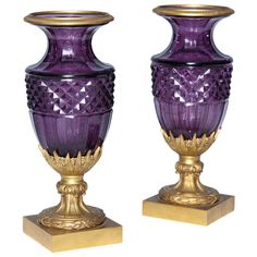 two purple glass vases sitting on gold bases