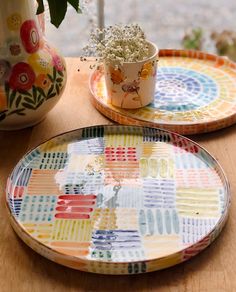 two colorful plates sitting on top of a wooden table next to a potted plant