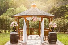 an outdoor gazebo with flowers and curtains on the top is surrounded by greenery