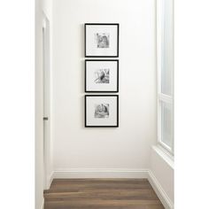 three black and white photos hang on the wall in an empty room with wood flooring