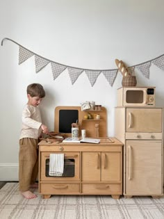 a young boy standing in front of a wooden play kitchen