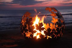 a fire pit on the beach at sunset with leaves carved into it's sides