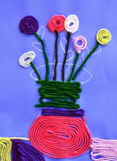 a vase filled with yarn and flowers on top of a blue tablecloth covered in multicolored thread