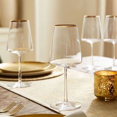 there are many wine glasses on the table with gold plates and silverware in front of them