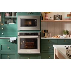 two ovens side by side in a kitchen with green cabinets and white counter tops