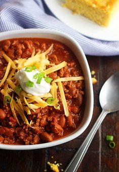 chili with cheese and sour cream in a white bowl on a wooden table next to a fork