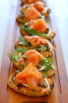 a wooden table topped with slices of bread covered in salmon and veggie toppings