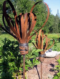 two metal sculptures sitting on top of a rock in the grass next to some plants