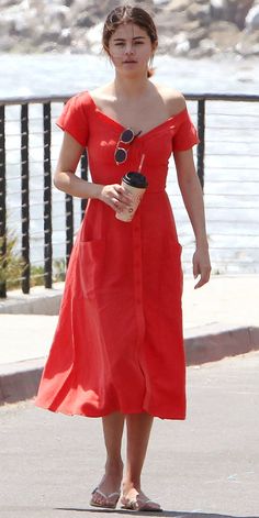 a woman in a red dress is walking down the street with her coffee and cell phone