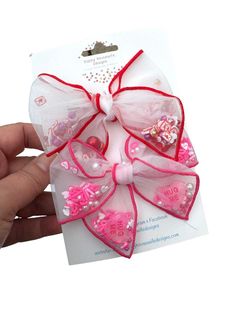 4 styles are available for these super cute confetti filled shaker Valentine’s Day hair bows on alligator clips. Pigtail sets are also available. Please allow for slight variations in fabric placement. Follow along for updates, giveaways, and more! Instagram: @happyhousewifedesigns Diy Valentines Hair Accessories, Valentines Hair Bows Diy, Valentines Bows Hair, Cute Confetti, Pink Hair Bow Accessories For Spring, Cute Adjustable Hair Accessories With Pink Bow, Alligator Clips, Mini Fashion, Alligator