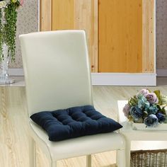 a chair and table in a room with wood flooring, white walls and blue cushions