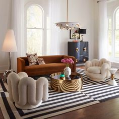 a living room filled with lots of furniture next to two large windows and a rug on the floor