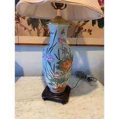 a blue vase sitting on top of a table next to a white lamp with flowers painted on it