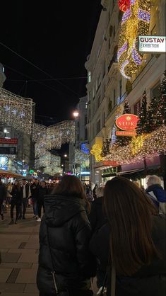 people are walking down the street in front of christmas lights