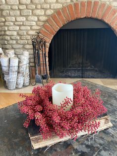 a candle and some flowers on a table in front of a brick fire place with a fireplace