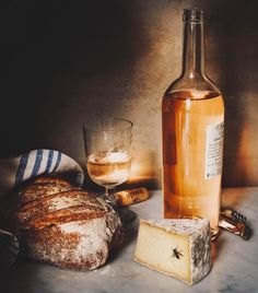 a bottle of wine next to bread and a glass on a table with other items