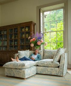 a woman laying on top of a couch next to a vase with flowers in it