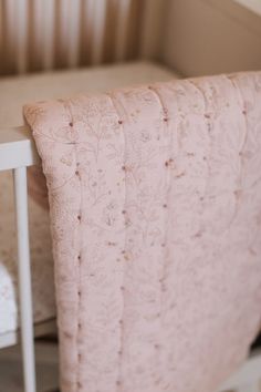 a baby crib with a pink blanket on it's back next to a white chair